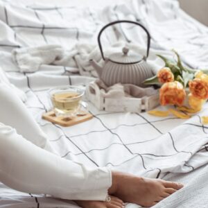 Woman reads in bed with tea, teapot and bouquet of flowers.